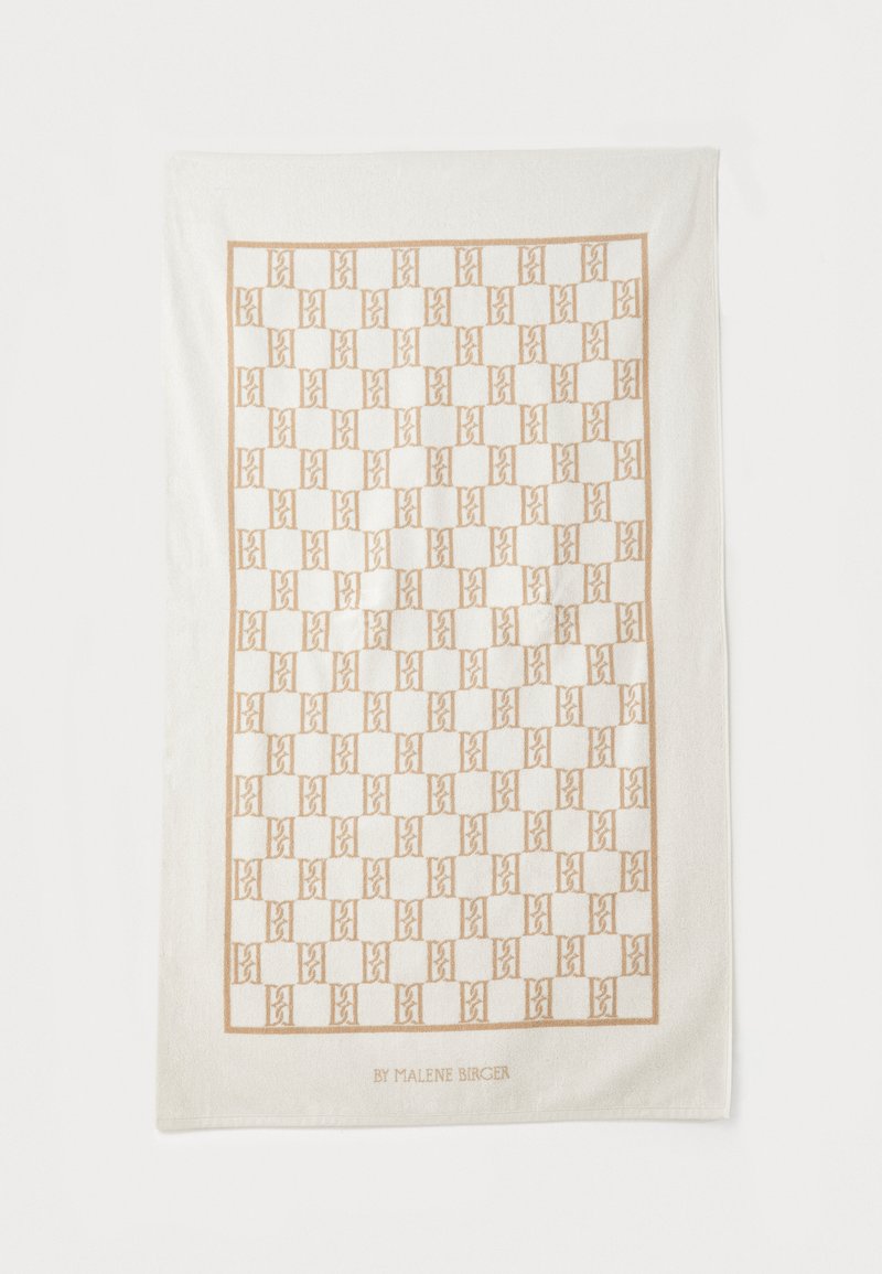 Asciugamano in cotone bianco con un motivo geometrico dorato e forme interconnesse. Testo in basso che recita "BY MALENE BIRGER."