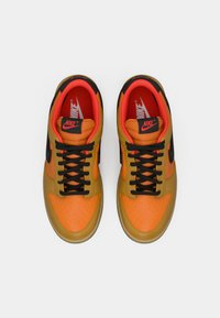 Nike sneakers featuring a blend of orange and yellow leather with black accents, black laces, and red interior lining. Round toe design.