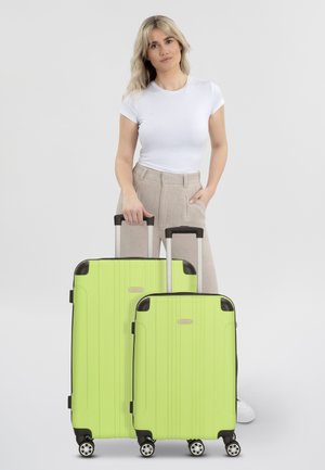 Twee limegroene harde koffer met geribbelde textuur, zwarte accenten en multidirectionele wielen, naast elkaar weergegeven, worden vastgehouden.