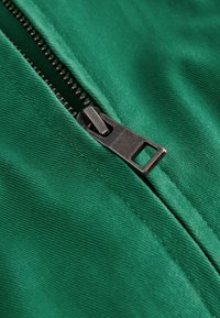 Gros plan d'une fermeture éclair en métal noir partiellement ouverte sur un tissu texturé vert.