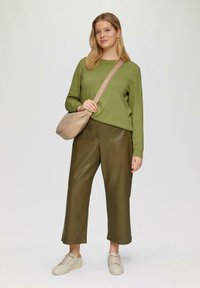 Olijfgroene gebreide trui, hooghangende olijfgroene neplederen broek en een beige schoudertas. Het model draagt lichte beige sneakers.