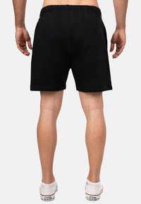 Zwarte katoenen shorts met een elastische tailleband, zijzakken en een recht model, gecombineerd met witte sneakers, gezien vanaf de achterkant.