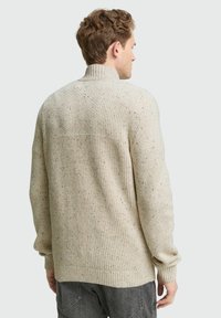 Beige gebreide trui met een hoge kraag, een textuurpatroon en gemêleerde accenten in verschillende kleuren. Losse pasvorm met geribde mouwen en onderrand.