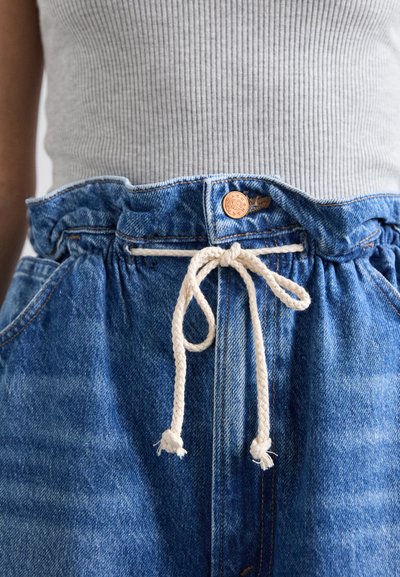 Απαλά μπλε τζιν σορτς με ελαστική μέση, διαθέτοντας λευκή κορδόνι και χαλκό κουμπί λεπτομέρεια στο μπροστινό μέρος. Υφασμα με υφή.