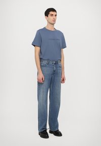 Light blue t-shirt with embossed "MICHAEL KORS" logo, paired with loose-fitting, light-wash denim jeans and black footwear. Simple design.