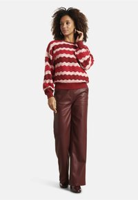 Red and pink zigzag-patterned sweater with ribbed cuffs, paired with high-waisted burgundy leather wide-leg pants. Smooth texture throughout.