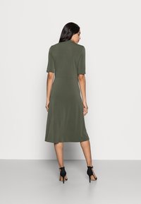 Vestido midi verde oliva feito de tecido macio, com mangas curtas e uma cintura ajustada, esvoaçando para uma saia ligeiramente ampla.