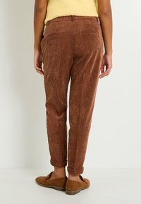 Pantalons en velours côtelé marron avec des rayures verticales, coupe fuselée et ourlets roulés. Comprend des poches arrière et un tissu texturé.