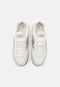 Bílé tenisky s šedými akcenty, svršek z kůže a textilu, kulatá špička, ploché tkaničky a podešev z gumy. Logo "New Balance" na jazyku.