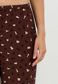 Pantalons bruns avec une taille extensible, ornés d'un motif léopard en noir et beige. Texture lisse, design ajusté.