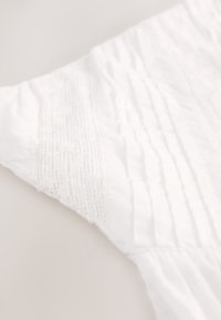 Tissu blanc présentant un panneau texturé avec des lignes verticales et un détail en dentelle le long du bord, mettant en valeur la douceur et un design complexe.