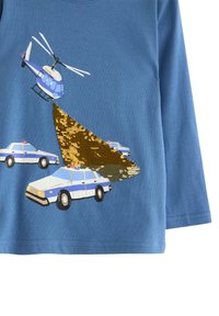 Blå langærmet skjorte med et design af en helikopter over politibiler og en guld-sekvenseffekt, der skaber visuel tekstur og detalje.