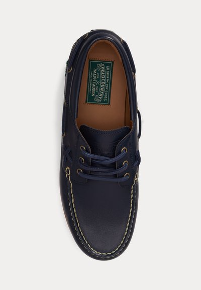 Granatowy skórzany but żeglarski z beżowym przeszyciem, wiązany z przodu, z zieloną etykietą Polo Country by Ralph Lauren wewnątrz.