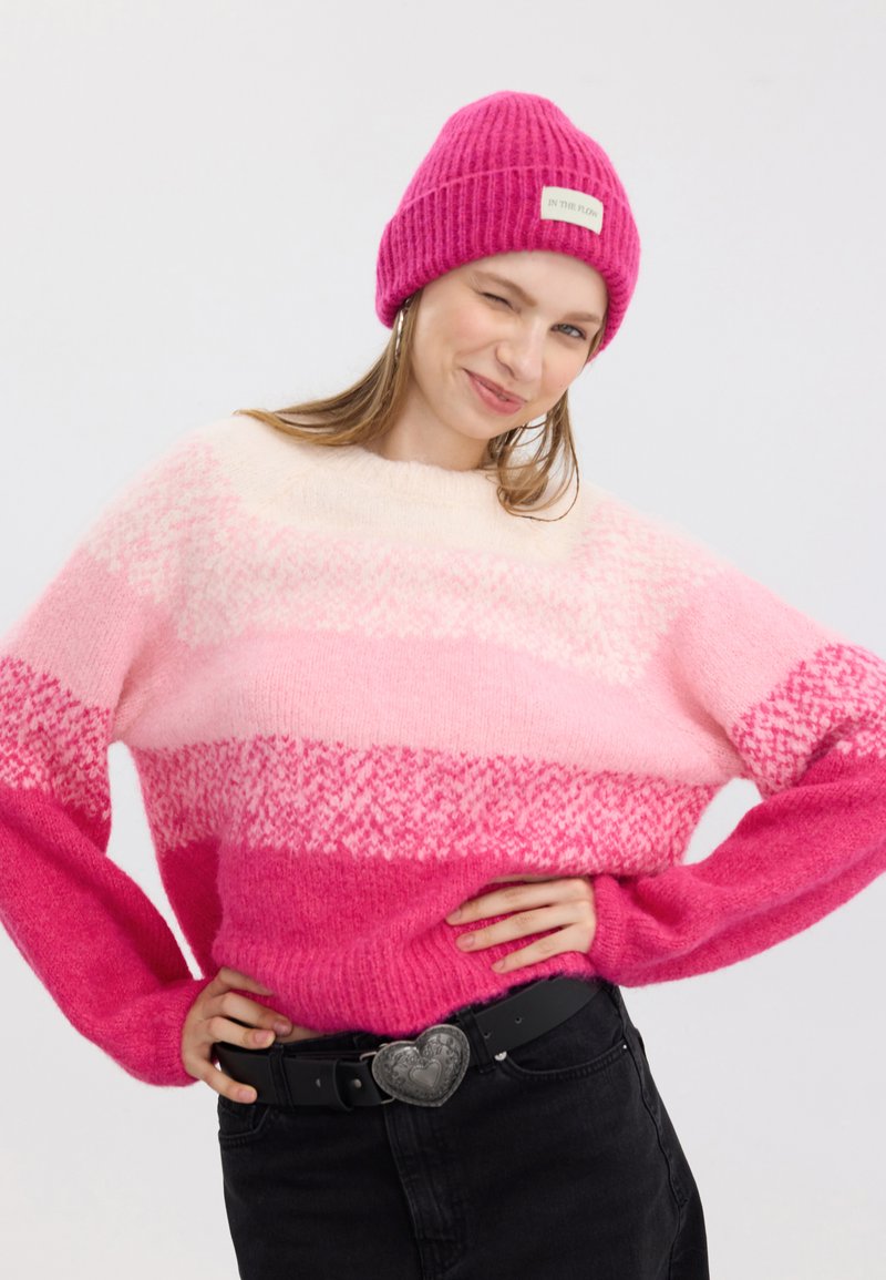 Rosa Strickpullover mit Farbverlaufstreifen, die von hellem Rosa bis leuchtendem Fuchsia reichen. Ein Paar rosa gerippte Mütze mit einem Etikett. Schwarzer Gürtel.