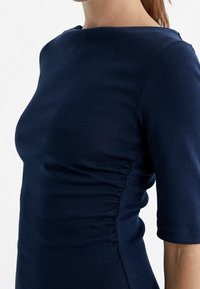 Granatowa dopasowana sukienka z wykrojem w kształcie łódki, krótkimi rękawami i marszczeniami po bokach, wykonana z gładkiego, elastycznego materiału.