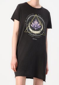 Czarna bawełniana sukienka typu T-shirt z krótkimi rękawami, z przodu z graficznym motywem kwiatu lotosu oraz geometrycznym wzorem w stonowanych kolorach. Asymetryczny dół.