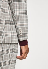 Grijs-witte geruite colbert met een contrasterende bordeauxrode manchet, vier knopen op de mouwen en een slim fit.