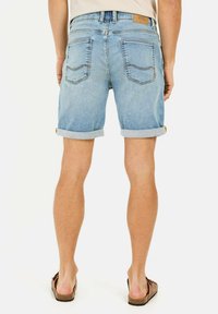Shorts en denim bleu clair avec des ourlets retroussés, dotés de poches arrière et d'une étiquette en cuir beige sur la ceinture. Portés avec des sandales marron.