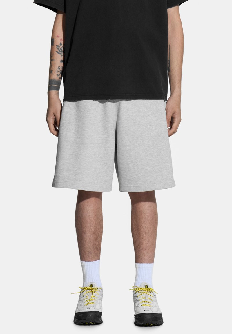 Szare krótkie spodenki dresowe o luźnym kroju, wykonane z miękkiego materiału. W zestawieniu z czarną, oversize'ową koszulką oraz strukturalnymi białymi i czarnymi sneakersami.