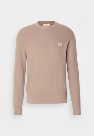 Maglione lavorato a maglia beige chiaro con maniche lunghe, scollatura a girocollo e un motivo testurizzato; presenta una piccola etichetta con logo sul petto.