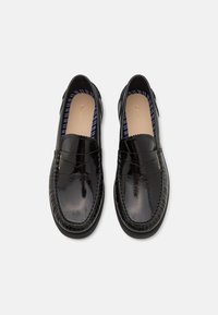 Mocasini din piele lăcuită neagră cu un design cusut pe vârf, căptușeală interioară cu dungi și branding aurit embosat pe lateral.