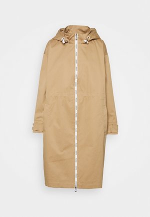 Impermeable largo beige con capucha y cremallera frontal blanca que presenta la marca "HUGO" repetida, puños ajustables y bolsillos laterales.