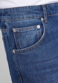 Denimjeans i djupblått med orange sömmar, med en liten metallisk logotyp på framfickan och en klassisk femficksdesign.