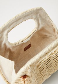 Vevd stråhåndveske med en beige linjerte innside, med runde håndtak og en subtil tekstur. Inkluderer et lærmerke inni.
