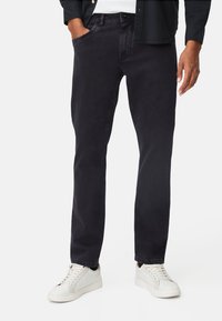 Donkergewaste spijkerbroek van denim, met een rechte pasvorm, contrasterende stiksels en voorzakken. Gecombineerd met witte sneakers.