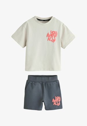 Ensemble composé d'un t-shirt crème à manches courtes et d'un short gris foncé avec des logos textuels roses "AllSaints London" sur la poitrine et la jambe du short.