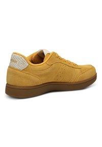 Baskets en daim jaune avec semelle marron, patch talon blanc texturé et design à lacets, vues de côté.