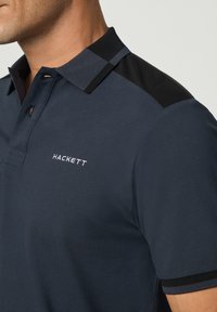 Námořnická polokošile s krátkým rukávem, strukturovaná tkanina, černé akcenty na ramenou a bílé vyšívané logo s nápisem "HACKETT."