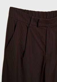Pantalon de costume marron foncé à fines rayures, avec plis, passants de ceinture et poches latérales, présenté de la taille jusqu'au milieu de la cuisse sur un fond clair.