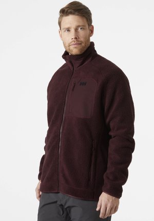 Chaqueta de forro polar en burdeos oscuro con un alto cuello, cremallera completa y un bolsillo en el pecho. Presenta una textura suave y bolsillos laterales.