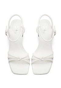 Weiße High Heels Sandalen mit quadrater Zehenpartie, die über geknotete Riemen und ein Slingback-Design verfügen. Glatte Textur mit dezentem Branding auf der Innensohle.