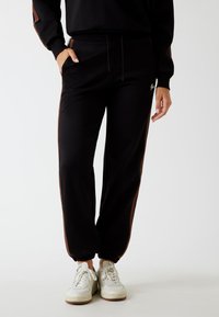 Zwarte joggingbroek met bruine zijstrepen, elastische tailleband en boorden, voorzien van een zijzak en een gladde, zachte stofstructuur.