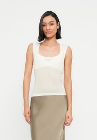 Αμάνικη κορυφή σε ανοιχτό ελεφαντόδοντο με στρογγυλή λαιμόκοψη, κατασκευασμένη από απαλό, αναπνεύσιμο ύφασμα με διακριτική υφή και εφαρμοστή σιλουέτα.