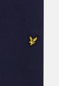 Marineblauwe gebreide stof met een klein geel geborduurd vogellogo, omrand met zwart, aan de linkerkant geplaatst.