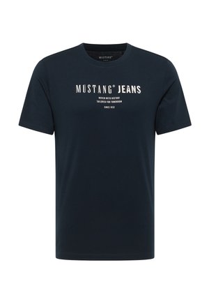Sötétkék pamut póló kerek nyakkal és rövid ujjal. Elöljárója a "MUSTANG JEANS" felirat fehér színben és egyéb márkázott részletek találhatók.