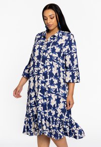 Langarmkleid mit einem blauen und cremefarbenen abstrakten Muster, mit Kragen, Knopfverschluss und Rüschensaum. Weiche Stofftextur.