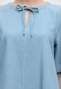 Φόρεμα από ανοιχτό γαλάζιο τζιν με κοντά μανίκια και μπροστινό άνοιγμα σε σχήμα κλειδαρότρυπας, δεμένο με φιόγκο από ύφασμα.