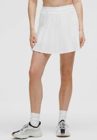 Jupe mini plissée blanche avec une large taille, associée à des chaussures de sport noir et blanc. Tissu texturé avec des plis nets.
