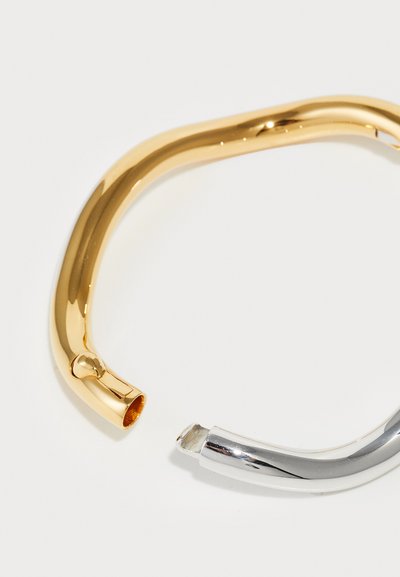 Brățară din metal aurit și argintie, cu o formă curbată, finisaj strălucitor, având un design despărțit în care cele două capete nu se conectează.