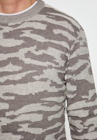 Pulover cu model de camuflaj gri și bej, cu guler rotund ribat și tricot texturat. Materialul pare moale și călduros.