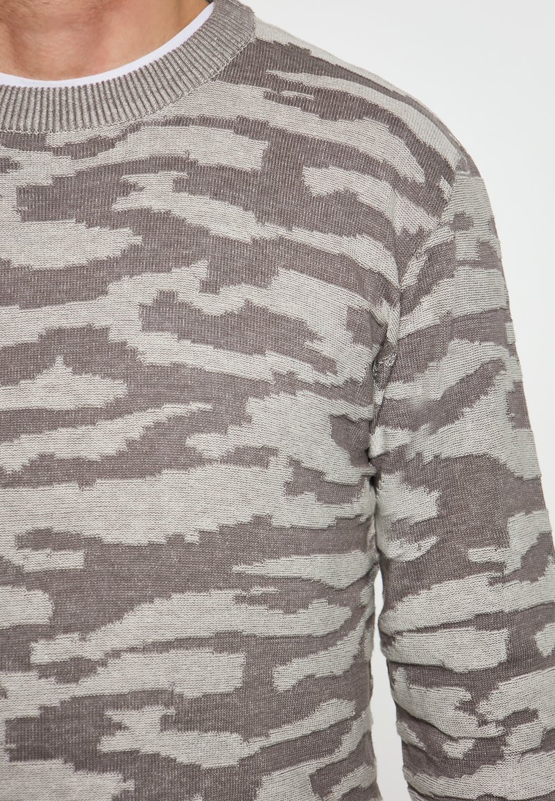 Pulover cu model de camuflaj gri și bej, cu guler rotund ribat și tricot texturat. Materialul pare moale și călduros.
