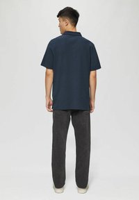 Navy blue polo shirt with short sleeves, made of smooth material. Paired with dark gray, loose-fitting pants and light shoes.