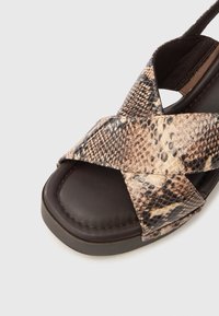 Σανδάλια με σχέδιο φίδι και σχέδιο λουριών που διασταυρώνονται, συνθετικό επάνω μέρος, μαλακό τακούνι σε σκούρο καφέ χρώμα και τετράγωνο σχήμα δαχτύλων.