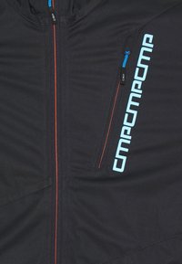 Schwarze Jacke mit vollem Reißverschluss und orangefarbigen Akzenten, einer kleinen Reißverschlusstasche und blauen Logodetails auf der Vorderseite. Glatte Stofftextur.