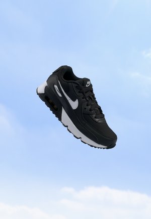 Baskets Nike Air Max noir et blanc suspendues dans les airs sur un fond de ciel bleu clair.