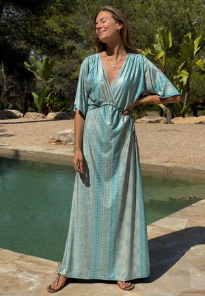 Duga tirkizna haljina s uzorkom, s V-izrezom i širokim rukavima, stegnuta u struku. Lagani materijal, glatka tekstura i lepršav dizajn.